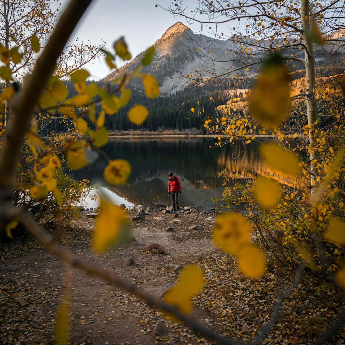 person in red jacket standing near lake during daytime